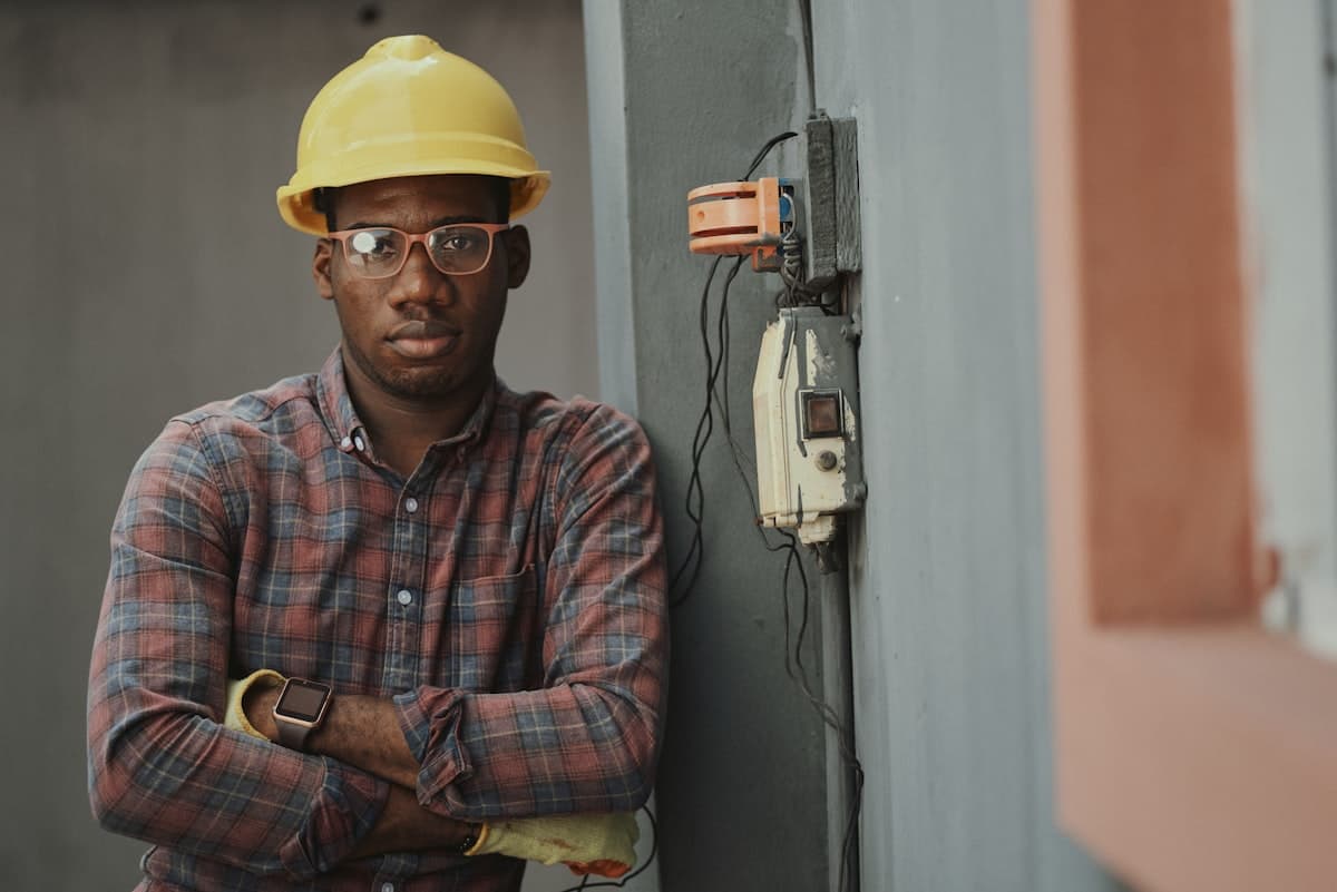 Worker in a hard hat and safety glasses standing beside an exterior electrical panel